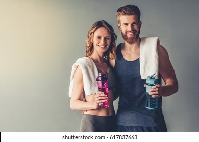 Beautiful young sports people are holding bottles of water, looking at camera and smiling, on gray background - Powered by Shutterstock
