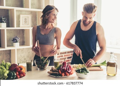 Beautiful young sports people are talking and smiling while cooking healthy food in kitchen at home