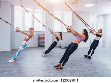 Beautiful Young Sports Women Are Working Out With TRX In Gym. Light Background