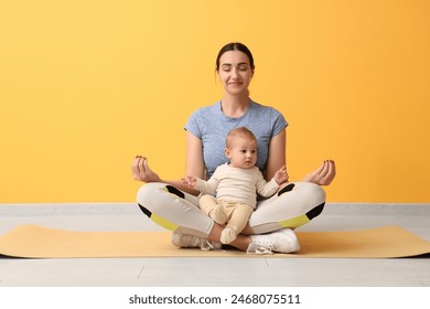 Beautiful young sporty woman with her little baby meditating near yellow wall - Powered by Shutterstock