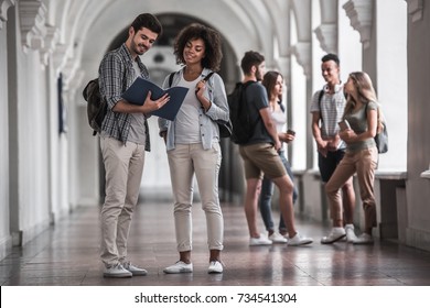 Schöne junge Studenten ruhen sich in der Universitätshalle auf, ein Paar im Vordergrund studiert etwas und lächelt