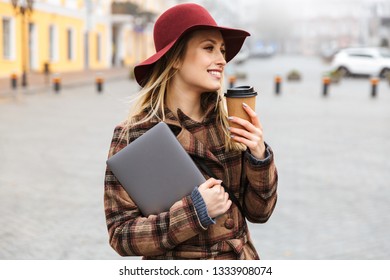 Beautiful Young Stylish Blonde Woman Wearing A Coat Walking Outdoors, Carrying Laptop Computer