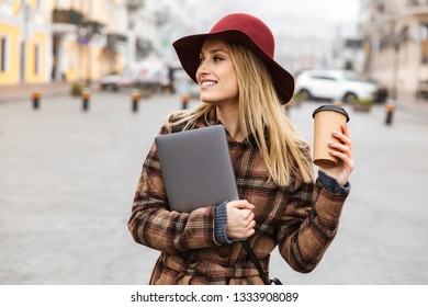 Beautiful Young Stylish Blonde Woman Wearing A Coat Walking Outdoors, Carrying Laptop Computer