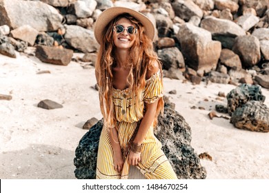 beautiful young stylish boho woman in elegant dress outdoors wearing hat and sunglasses at sunset