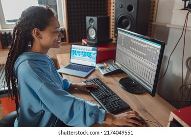 Beautiful young stylish female African audio engineer and producer working in music recording studio creating cool song