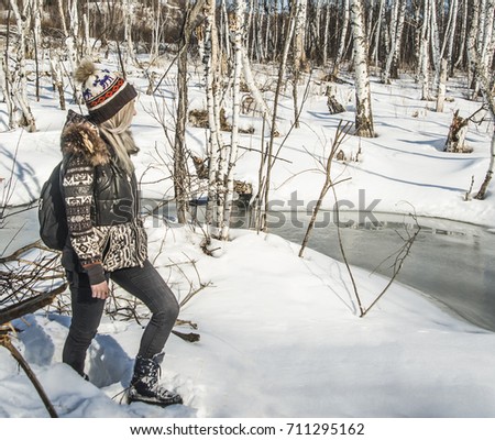 Beautiful young stylish woman walking along river. nature in winter. beautiful young female hiker with backpack walking on scenic background with winter river. dry dead trees. blond girl