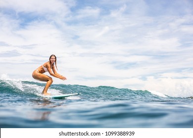 Beautiful young surfer girl in sexy pink bikini surfing longboard on the big waves and look to camera. Modern family lifestyle, people water sport adventure camp and extreme swim on summer vacation.