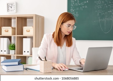 Beautiful young teacher with laptop sitting at table in classroom