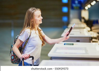 Beautiful young tourist girl with backpack and carry on luggage in international airport at check-in counter, giving her passport to an officer and waiting for her boarding pass