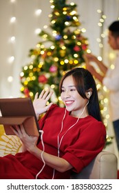 Beautiful Young Vietnamese Woman Video Calling Her Friends When Boyfriend Decorating Christmas Tree In Background