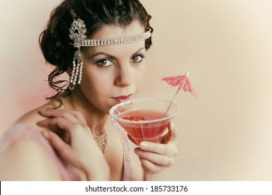 Beautiful young vintage 1920s woman with headband and flapper dress drinking a cocktail