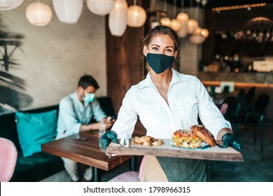Schöne junge Kellnerin mit Gesichtsschutzmaske, die köstliche Burger bis mittelalterliche männliche Kunden serviert. Corona Virus und kleine Unternehmen ist offen für Arbeitskonzept.