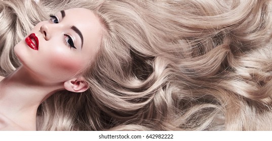 Beautiful young well-groomed girl lies - close-up. Long light shiny healthy well-groomed long hair. Advertising of hair care, cosmetics, beauty. Makeup - red lips, black arrows, mascara.