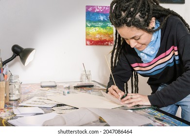 Beautiful Young White Hispanic Latin Art Director Girl With Casual Clothes And Dreadlocks Designing A Cinematic Mockup On Her Work Table Illuminated By A Lamp In Her Workshop