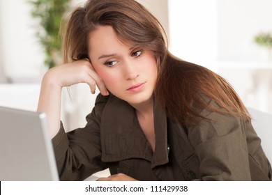 Beautiful young white woman working at desk wearing green casual jacket with long brown hair.