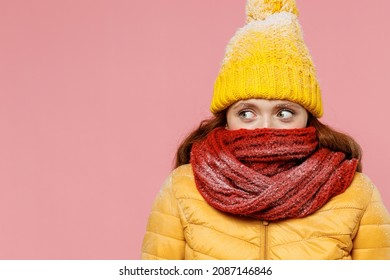 Beautiful young woman 20s years old wears yellow jacket hat mittens looking aside cover close hiding mouth with scarf wrapped around neck isolated on plain pastel light pink background studio portrait