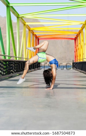 Beautiful young woman acrobat posing on the rainbow bridge