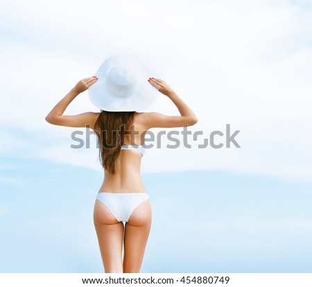 Beautiful, young woman in alluring bikini posing with a hat on the beach. 