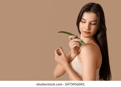 Beautiful young woman with aloe vera leaf on beige background