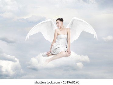 Beautiful young woman as angel sitting on a cloud, with white heart and halo