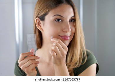 Beautiful young woman applying acne treatment anti-pickel patch on a pimple in bathroom at home