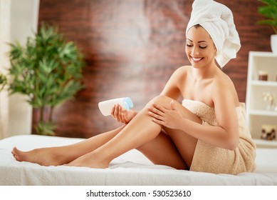 Beautiful young woman applying body lotion. 