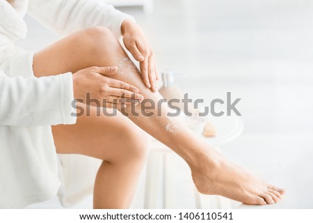 Beautiful young woman applying body scrub at home