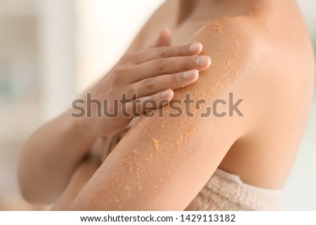 Beautiful young woman applying body scrub at home, closeup