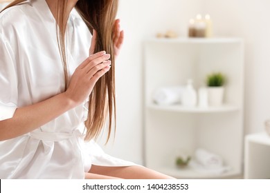 Beautiful young woman applying coconut oil on hair at home