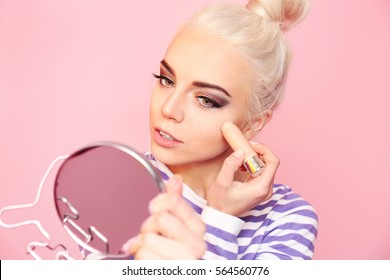 Beautiful young woman applying concealer stick