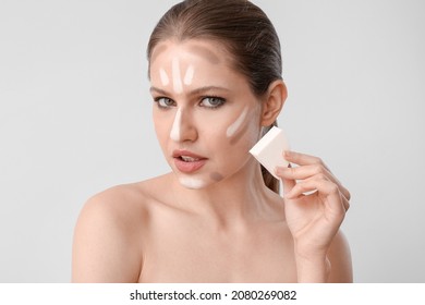 Beautiful Young Woman Applying Contouring Makeup Against Light Background