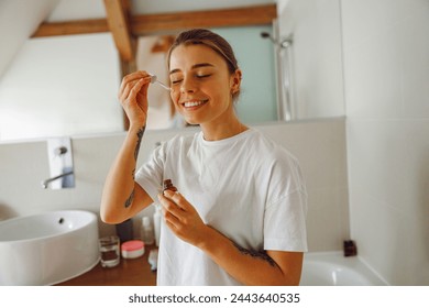 Beautiful young woman applying cosmetic serum onto her face in bathroom. Facial Skincare - Powered by Shutterstock