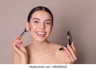 Beautiful Young Woman Applying Face Powder With Brush On Dusty Rose Background