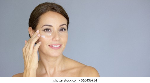 Beautiful young woman applying face cream
