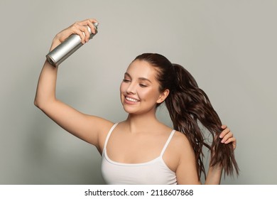Beautiful young woman applying hair spray on her hair.