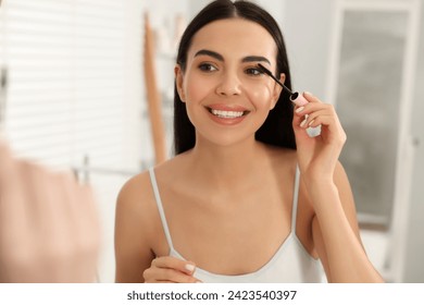 Beautiful young woman applying mascara near mirror in bathroom - Powered by Shutterstock