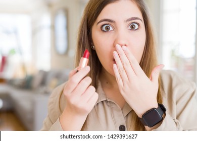Beautiful young woman applying red lipstick cover mouth with hand shocked with shame for mistake, expression of fear, scared in silence, secret concept