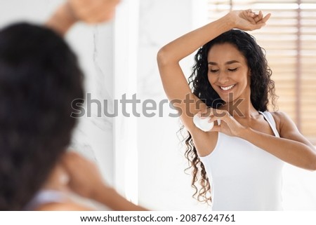 Beautiful Young Woman Applying Roller Deodorant To Armpit Zone In Bathroom, Smiling Millennial Female Using Antiperspirant For Underarms For Sweat Protection, Making Daily Beauty Routine Near Mirror