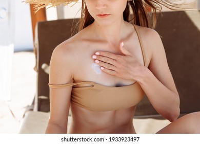 Beautiful young woman applying suntan lotion at sea with copy space. Tanned girl in bikini applying sunscreen on shoulder at tropical beach. Woman protecting skin with sunblock cream from UV.