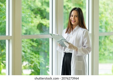 A Beautiful Young  Woman Asian Scientist Keep Looking Clipboard  To Analysis And Research Biology Chemistry And Medicine In Bright Modern Laboratory Or Technology Medical Room With Tree Background.