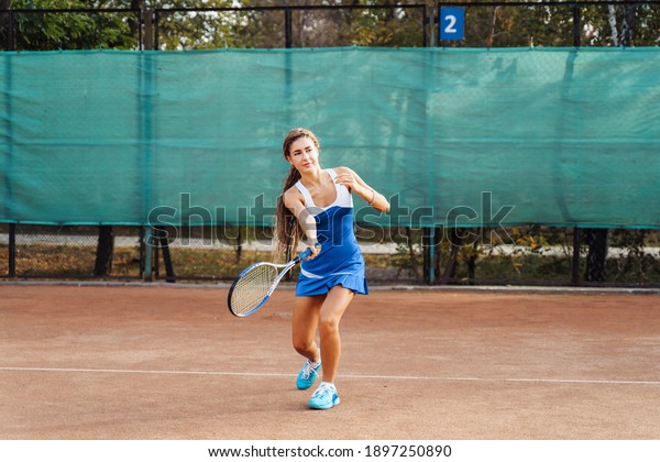 Beautiful, young woman athlete enjoys spending\
time on the tennis court. Powerful blow forehand. Preparing to\
receive the ball from the opponent. As focused and collected as\
possible.