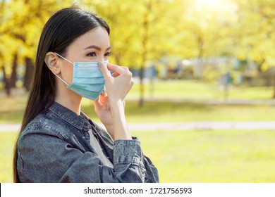 A Beautiful Young Woman Is Attaching Her Medical Mask While She Is Outside In A City Park. Communicate Or Debate About Mask Usage While Being Outside.