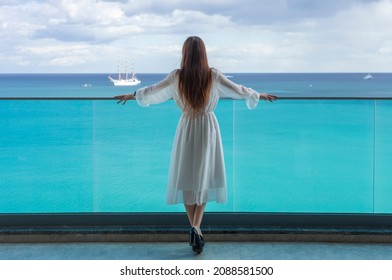 beautiful young woman from the back stands on the balcony and looks at the sea