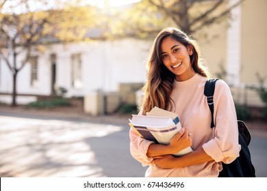 Beautiful young woman with backpack and books outdoors. College student carrying lots of books in college campus.