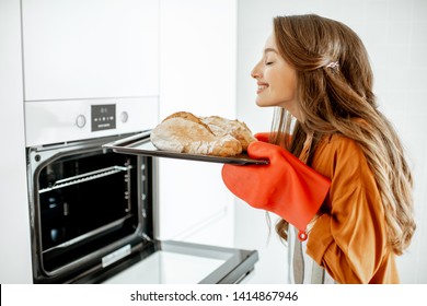 Beautiful Young Woman Baking Bread In The Oven At The Modern White Kitchen At Home