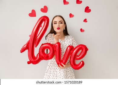 Beautiful young woman with balloon in shape of word LOVE and hearts on light background. Valentine's Day celebration