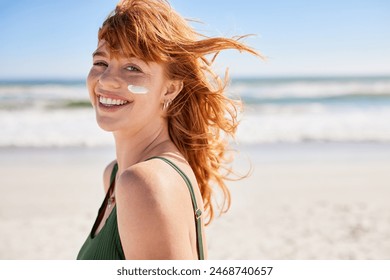 Beautiful young woman at beach with sunscreen on face looking at camera. Beauty girl with red hair enjoying summer holiday while applying suntan lotion at sea on cheek with copy space. - Powered by Shutterstock