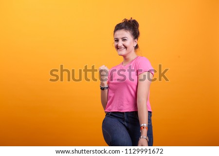 Beautiful young woman being victorius with pink t-shirt over yellow background in studio