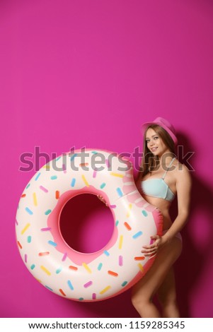 Beautiful young woman in bikini with inflatable ring against color background