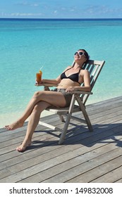 Schöne junge Frau in Bikini, die auf einer Liegestühle liegt, mit einem Drink am Meer